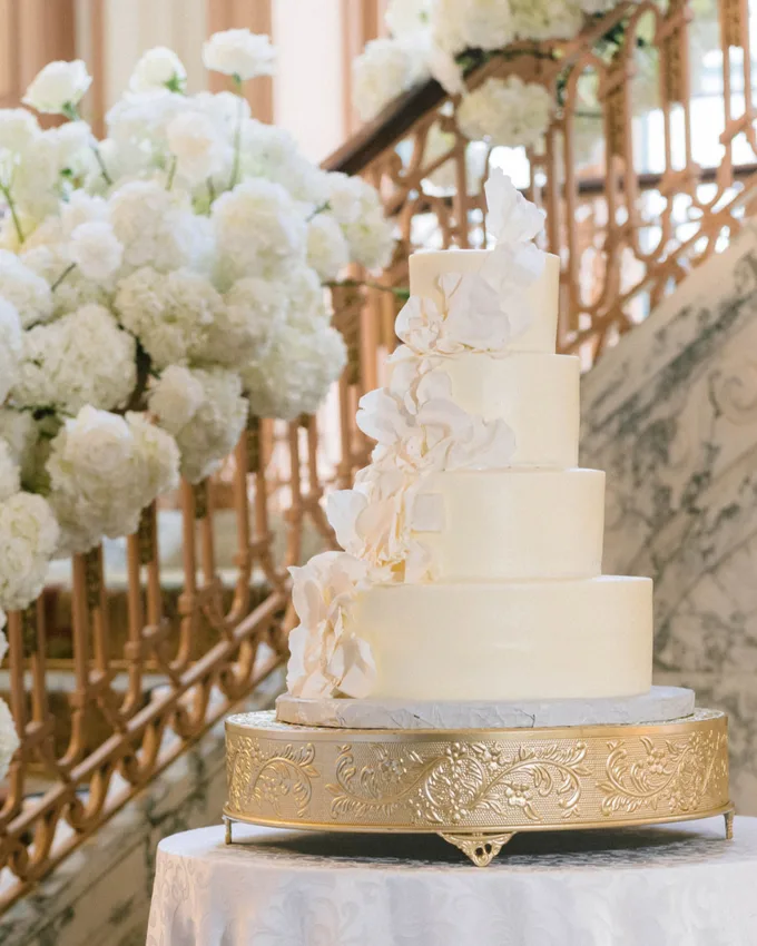 Tiered white wedding cake with cascading sugar roses on a gold stand