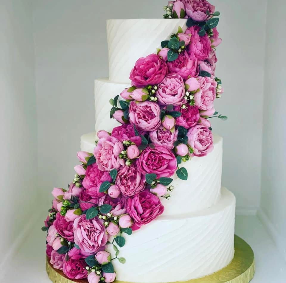 A white wedding cake cascading with vibrant pink blooms, suited to fruit-forward flavors like strawberry at Sweet Escape Cake Company in Indianapolis.
