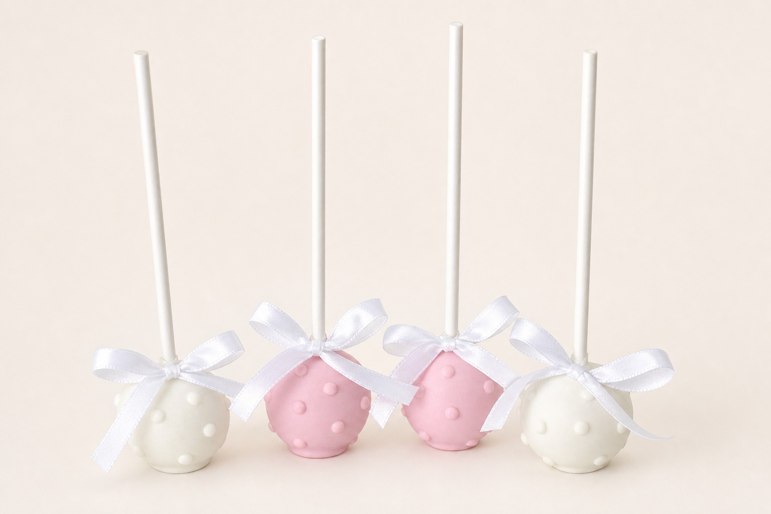 White and blush wedding cake pops with ribbon bows for a wedding dessert table by Sweet Escape Cake Company.