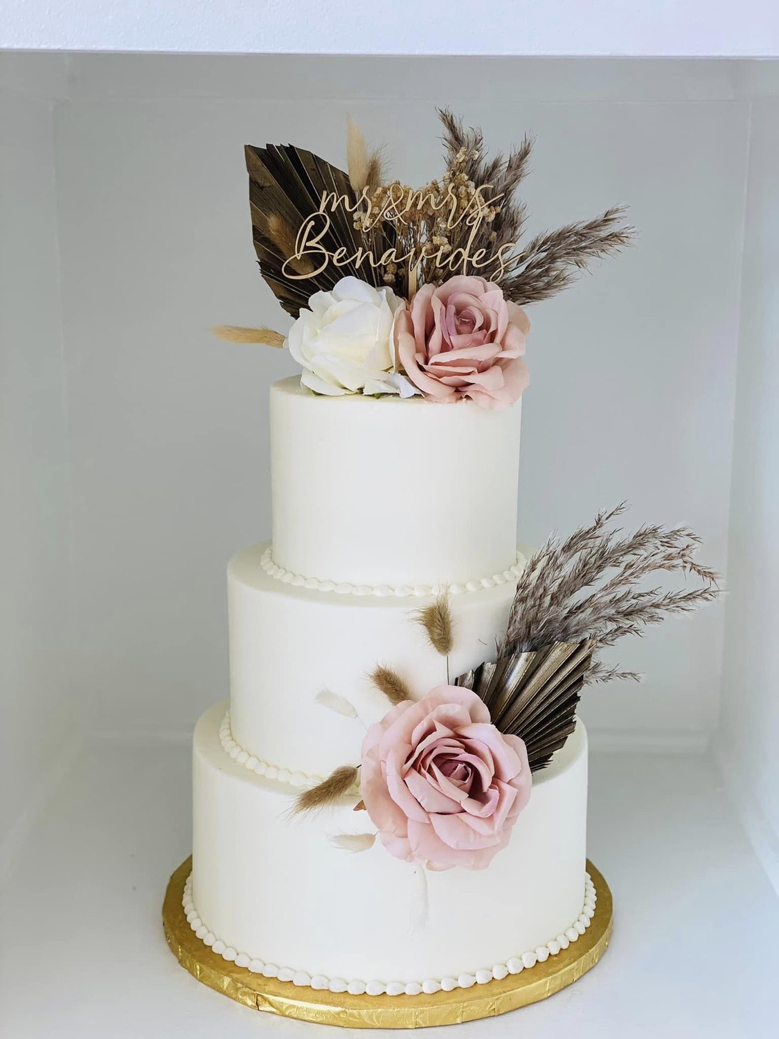 A three-tier white wedding cake with pink and white roses and pampas grass, styled for an outdoor summer Indiana wedding by Sweet Escape Cake Company in Indianapolis.