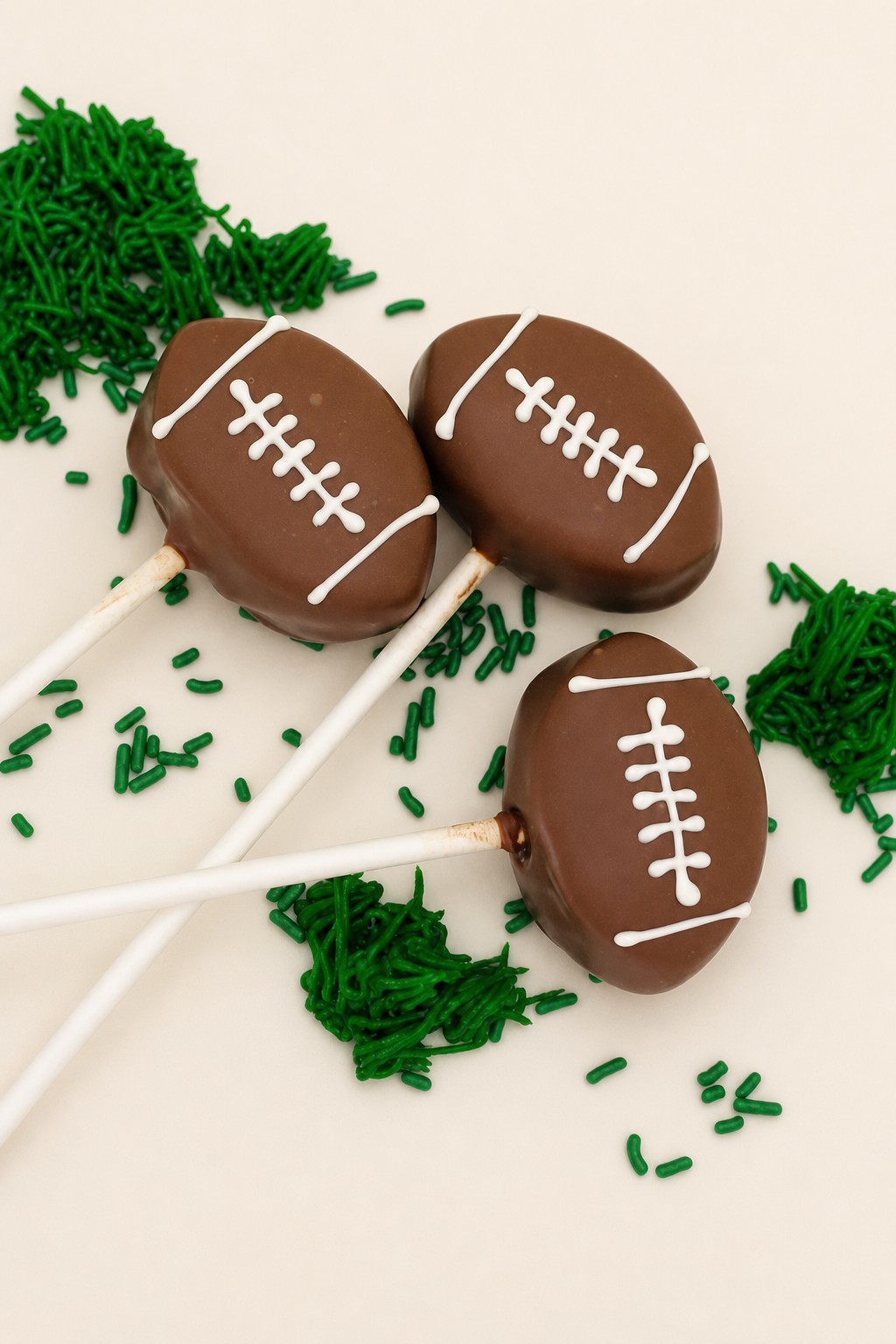 Chocolate football cake pops with piped white laces and green field sprinkles, football cake pops from Sweet Escape Cake Company.