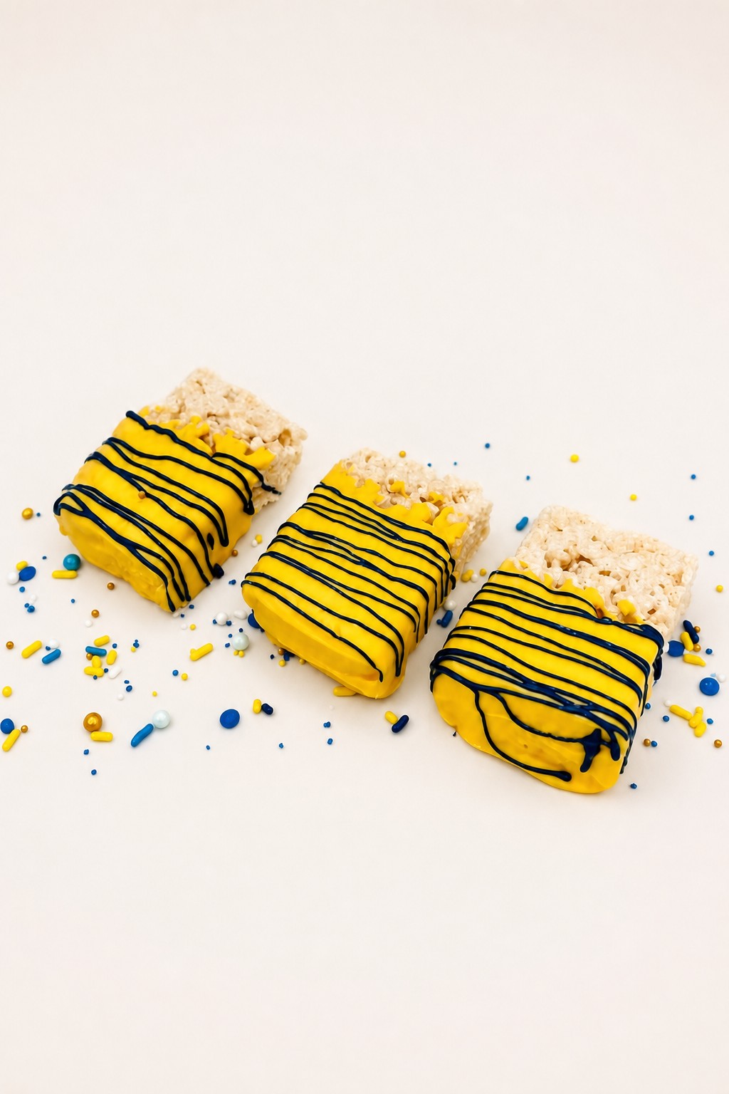 Rice krispie treats dipped in yellow candy coating with navy stripes, team color tailgate desserts from Sweet Escape Cake Company.