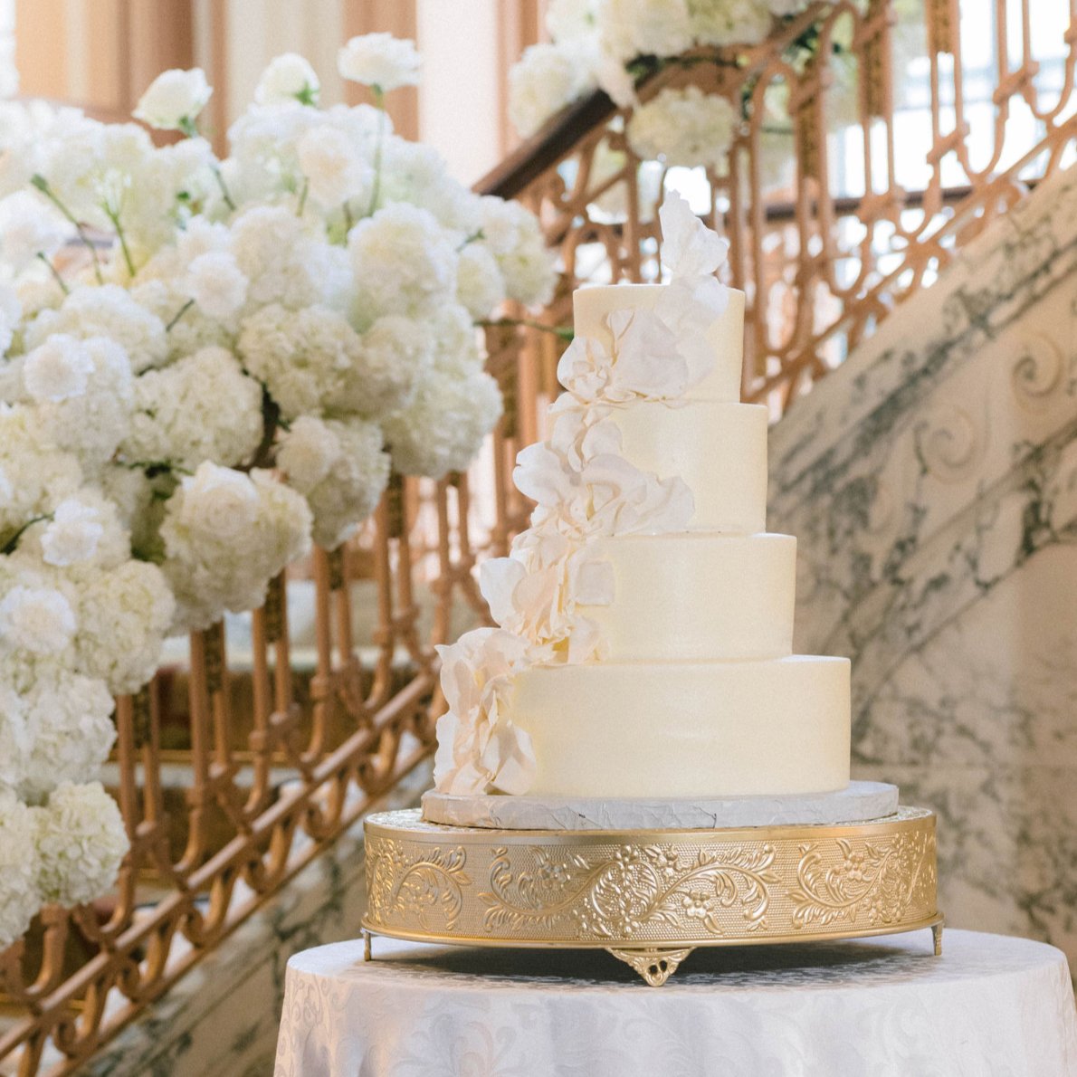 A tall cream buttercream wedding cake on a gold stand, one of the 2026 wedding cake trends by Sweet Escape Cake Company in Indianapolis.