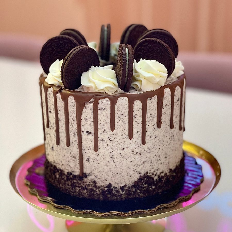 A delicious single-tier round Oreo themed birthday cake featuring a chocolate drip, white cookies and cream buttercream frosting, and whole 