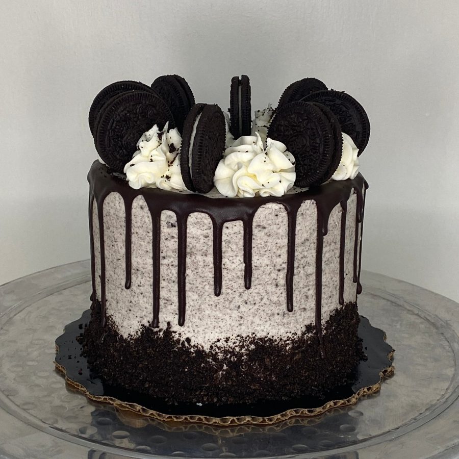 A delectable single-tier cookies and cream cake featuring a rich chocolate drip, whipped cream dollops, and whole Oreo cookies adorning the 