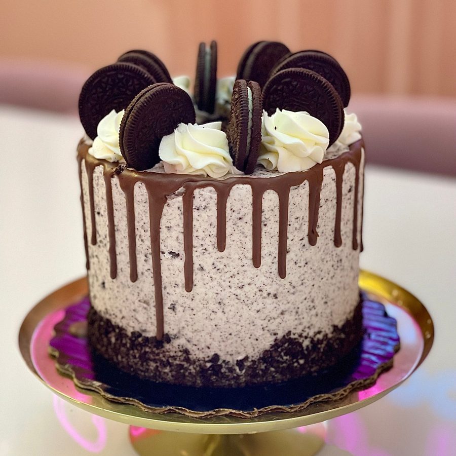 A single-tier round Oreo cookies and cream drip cake featuring white buttercream with cookie crumbs, chocolate ganache drip, and whole Oreo 