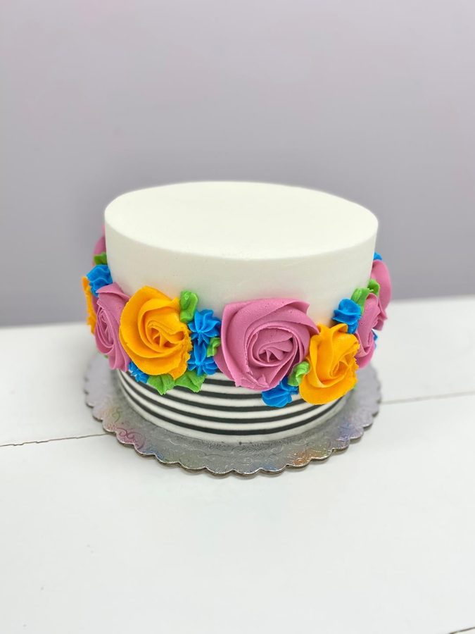 A single-tier round white buttercream cake featuring vibrant piped floral decorations and a bold black and white striped base.