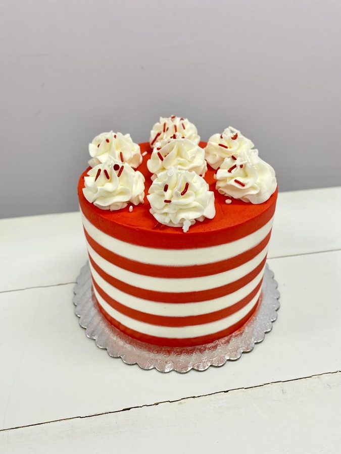 A festive round single-tier cake decorated with alternating horizontal red and white buttercream stripes and topped with white piped rosette