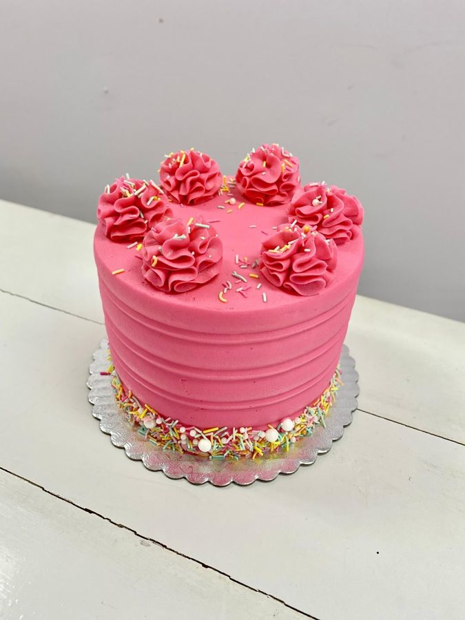 A vibrant pink single-tier round buttercream cake featuring horizontal ridged texture on the sides, topped with piped pink buttercream swirl