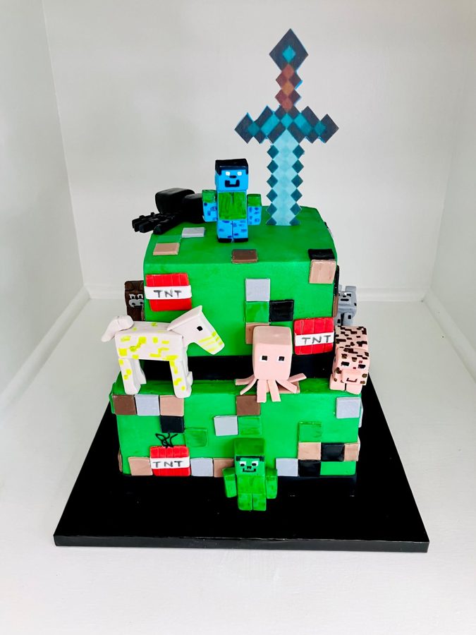 A vibrant two-tier square Minecraft-themed birthday cake featuring various sculpted fondant characters like Steve, Creeper, pig, horse, and 
