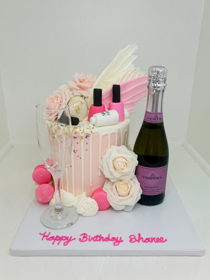 A elegant pink and white drip birthday cake decorated with pink macarons, various sugar flowers, gold leaf, purple sprinkles, and fondant na
