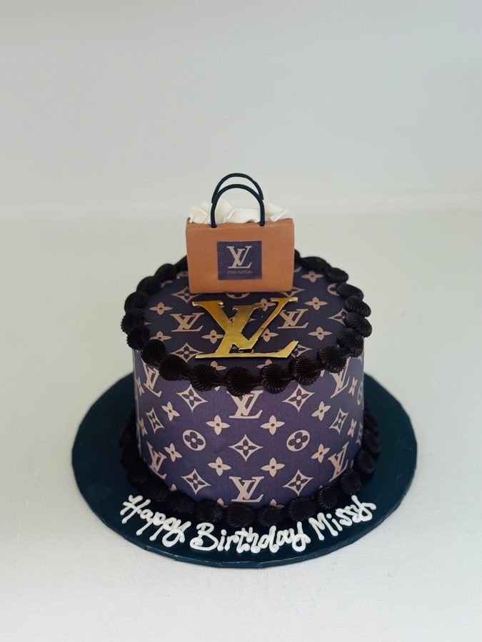 A single-tier Louis Vuitton themed birthday cake featuring a dark purple monogram edible image, a gold LV logo, and a mini shopping bag topp