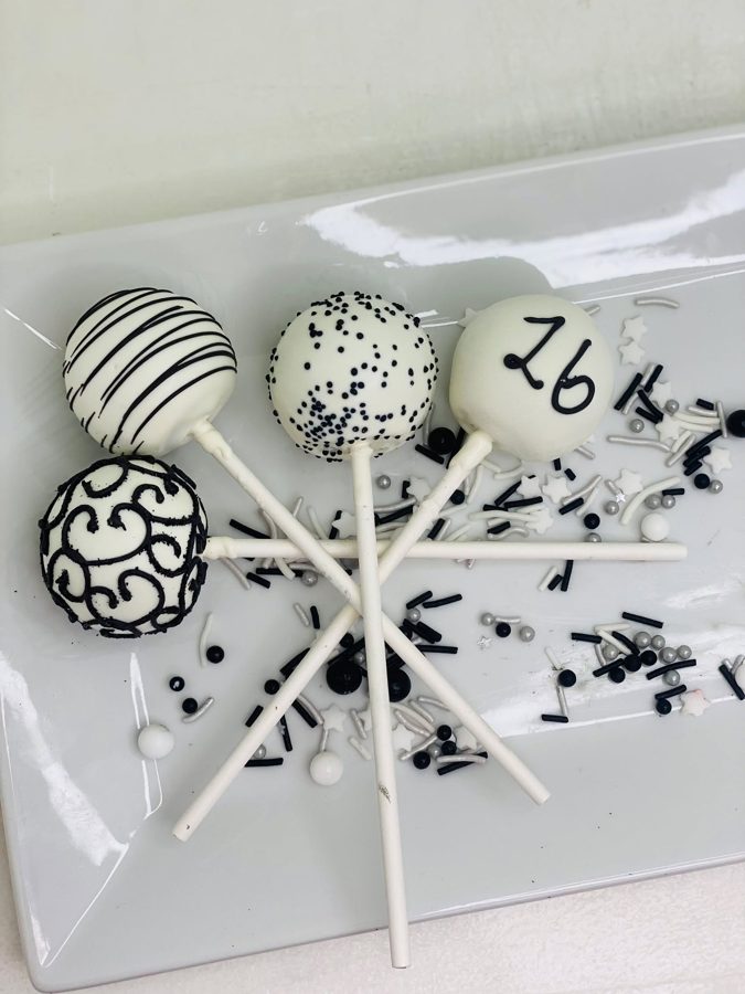 Elegant black and white cake pops with various designs including stripes, polka dots, intricate swirls, and a hand-drawn '26' numeral, finis