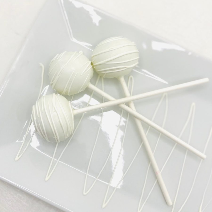 Three elegant white cake pops with delicate white drizzle presented on a white plate.