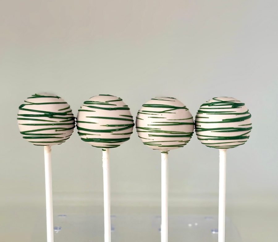 Four light-colored cake pops decorated with abstract dark green horizontal stripes or drizzles, presented on white sticks.