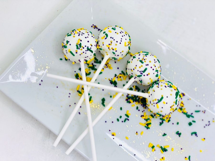White cake pops on sticks, decorated with green, purple, and gold sprinkles, perfect for a Mardi Gras celebration.