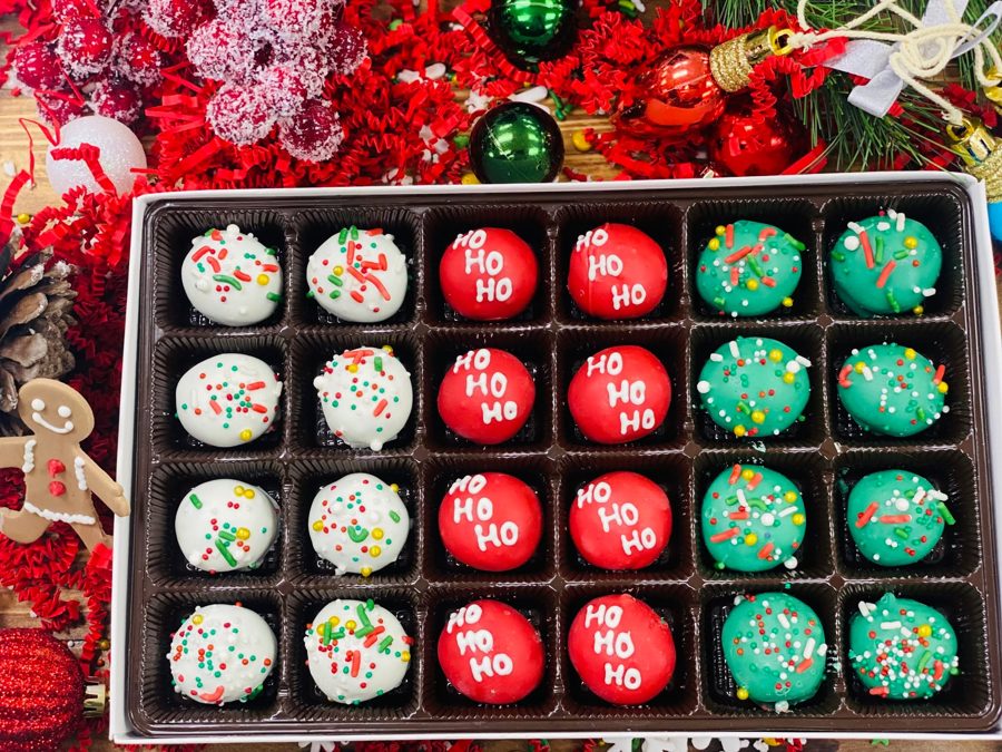 A festive assortment of Christmas-themed cake pops, including red ones with 'HO HO HO' in white royal icing, and white and green ones covere