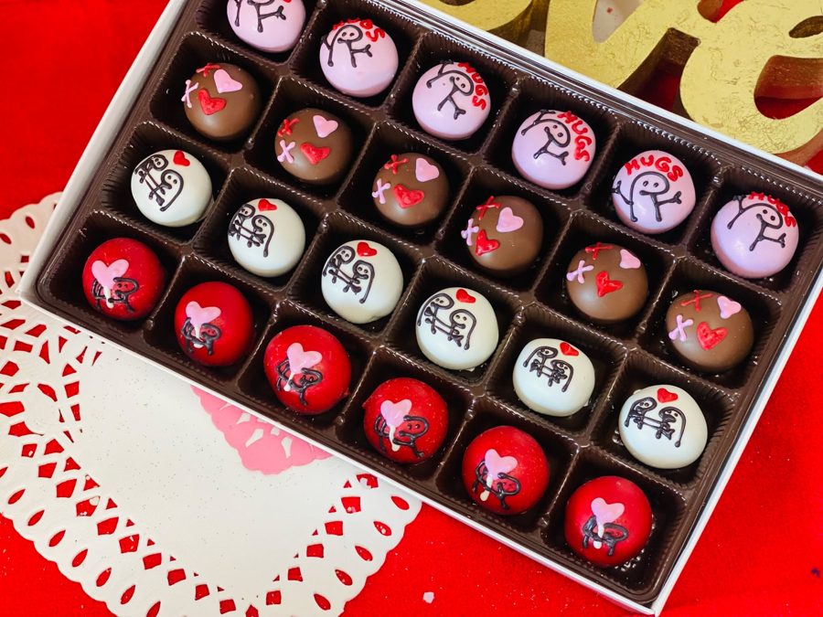 A box of festive cake pops featuring a mix of red, pink, white, and chocolate-flavored coatings, each adorned with sweet designs like hearts