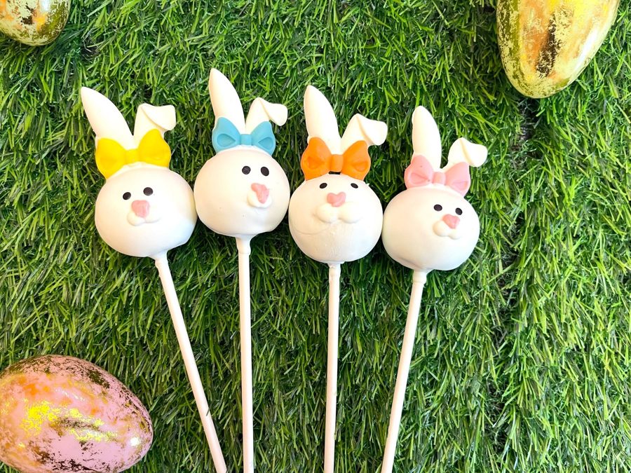 Four adorable white bunny cake pops, each featuring a colorful bow in yellow, light blue, orange, or pink, perfect for an Easter celebration