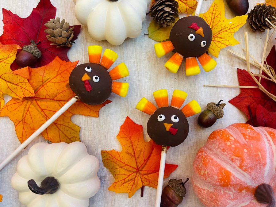 Thanksgiving turkey cake pops decorated with candy corn feathers and candy details, displayed with various fall harvest decorations.