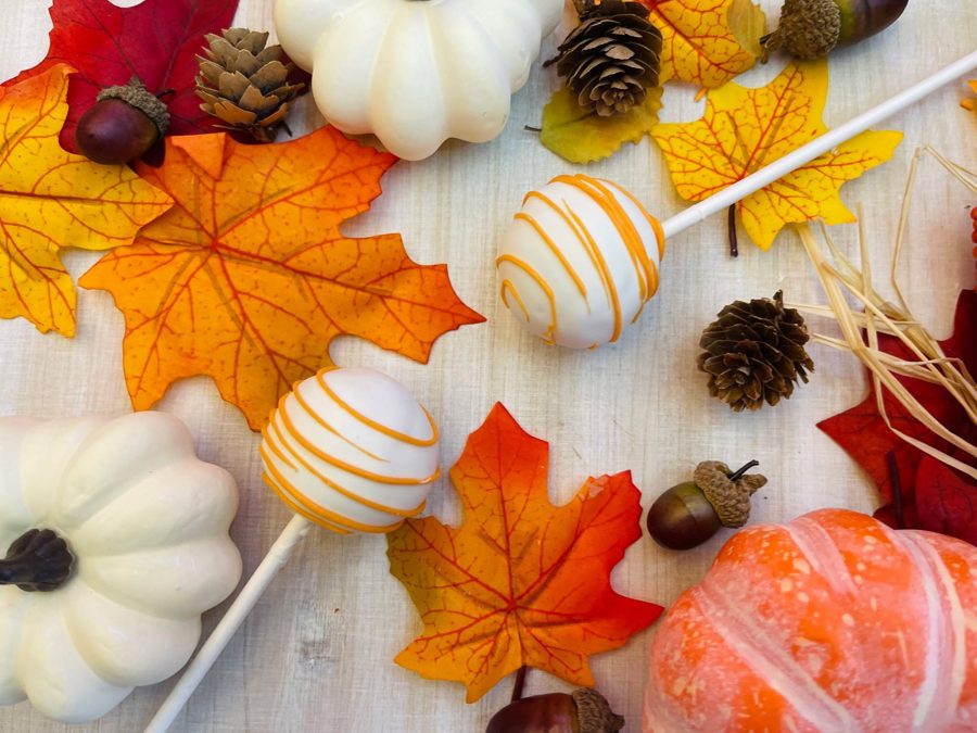 White cake pops decorated with orange stripes, perfect for an autumn or fall-themed celebration surrounded by fall leaves and pumpkins.