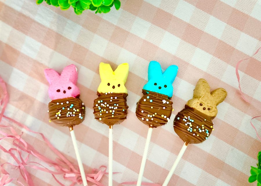A set of colorful marshmallow Peeps, including pink, yellow, blue, and brown, dipped in chocolate with pastel sprinkles, served on sticks, p