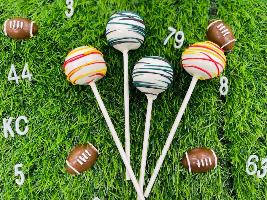 Football-themed cake pops with white icing and colorful red, yellow, green, black, and teal drizzles, displayed with chocolate footballs and