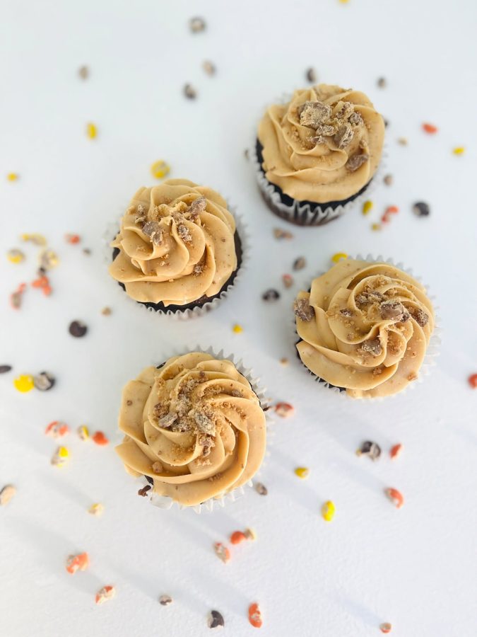 Delicious chocolate cupcakes topped with swirled tan or peanut butter-colored buttercream frosting and crunchy candy crumbles, scattered on 