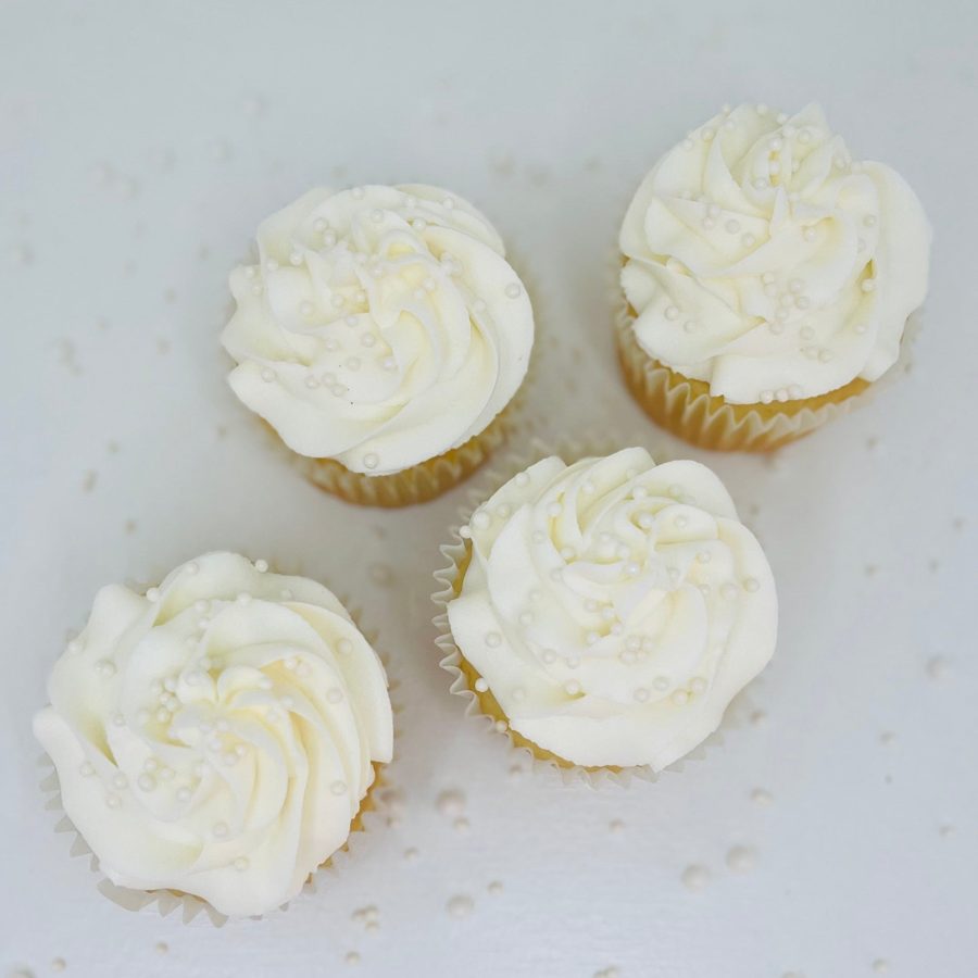 Elegant white cupcakes topped with swirled white buttercream frosting and small white pearl sprinkles, perfect for a wedding or special occa