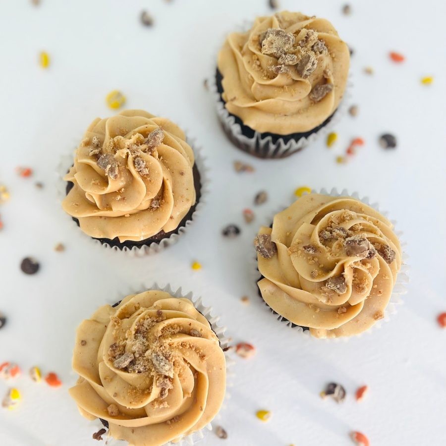 Four chocolate cupcakes topped with a swirl of light brown peanut butter flavored buttercream and a generous sprinkle of crushed candy piece