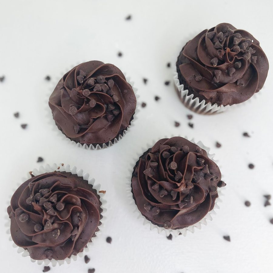 Four decadent chocolate cupcakes topped with rich, swirled chocolate buttercream frosting and mini chocolate chips, presented on a clean whi