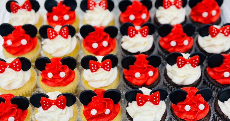 An assortment of Mickey and Minnie Mouse themed cupcakes featuring red and white buttercream frosting, black fondant ears, and red polka dot