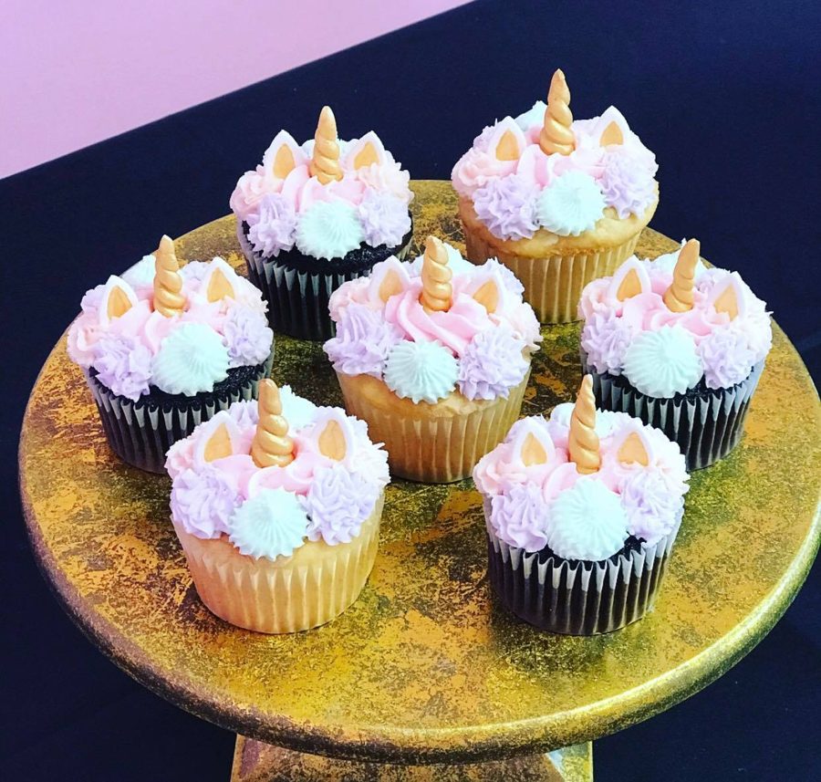 A collection of unicorn cupcakes featuring pastel pink, purple, white, and mint green buttercream frosting, topped with gold unicorn horns a