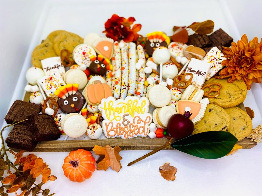 A festive Thanksgiving dessert bar featuring an assortment of fall-themed decorated cookies, turkey cake pops, pumpkin pie cookies, macarons