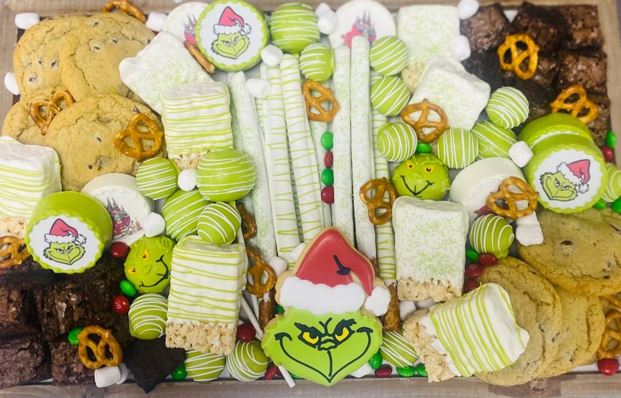A festive Grinch-themed dessert bar featuring a variety of treats including chocolate chip cookies, brownies, chocolate-covered pretzels, Gr