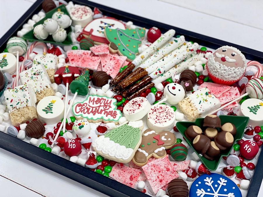 A festive Christmas dessert board featuring a variety of holiday-themed cookies, cake pops, chocolate-covered pretzels, marshmallows, candie