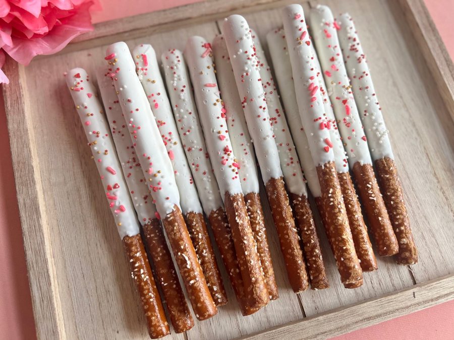 White chocolate-dipped pretzel rods generously adorned with a mix of pink, white, and gold sprinkles, including small heart shapes, perfect 