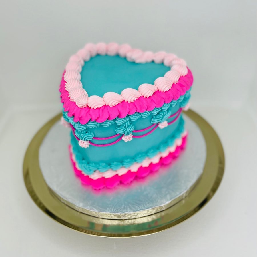 A vibrant heart-shaped cake with teal and hot pink buttercream frosting, featuring ruffle and swirl piping designs.
