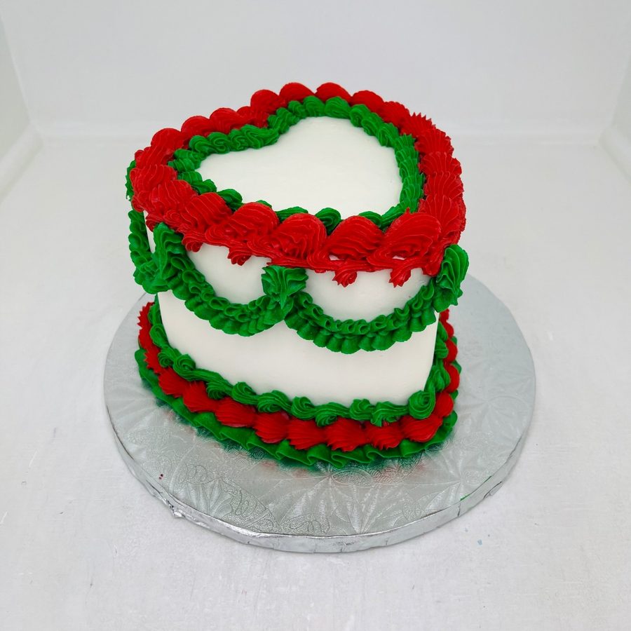 A heart-shaped white cake decorated with festive red and green buttercream ruffles and swirls, ideal for a holiday celebration.