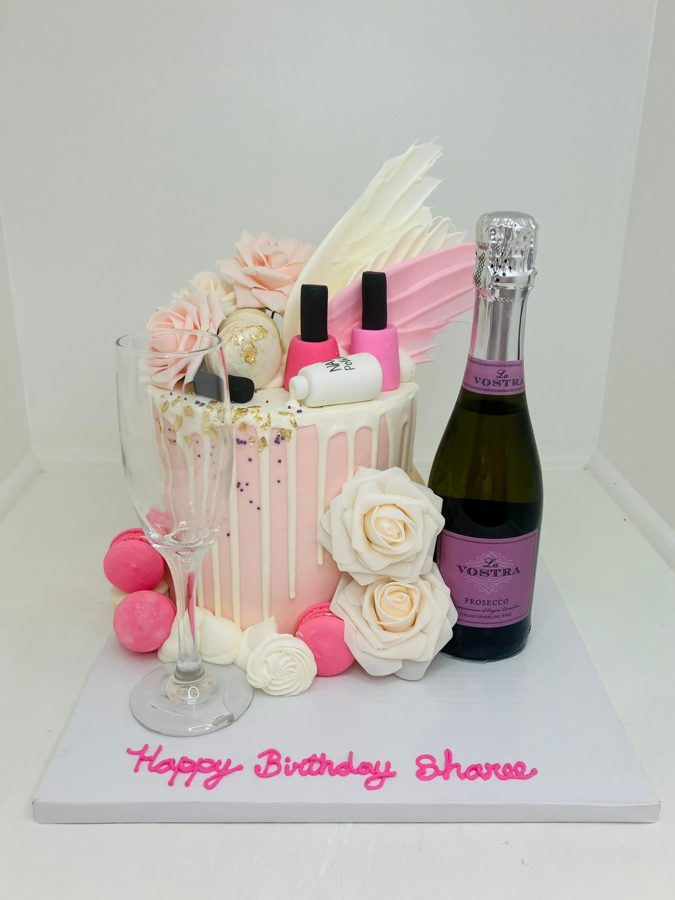 A elegant single-tier pink and white drip birthday cake adorned with fondant roses, gold leaf, purple sprinkles, pink macarons, and miniatur