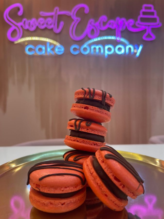 A stack of vibrant orange macarons filled with dark chocolate ganache and drizzled with dark chocolate on a golden tray.