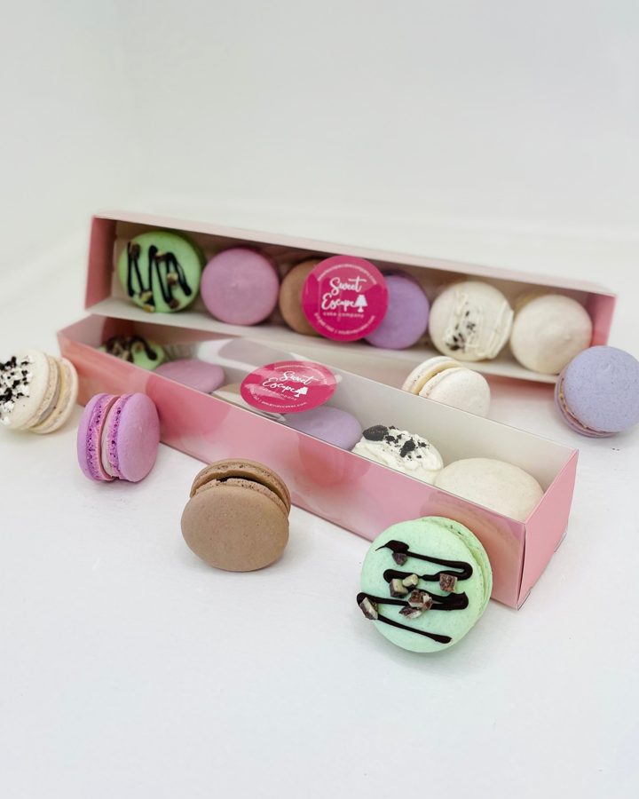 A vibrant assortment of pastel-colored macarons, some featuring chocolate drizzles and various toppings like cookie crumbs, presented in two