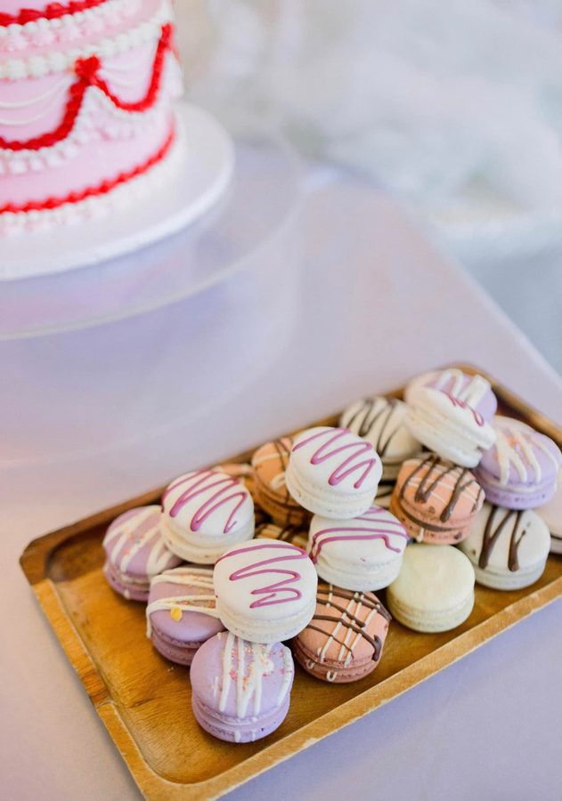A wooden tray filled with an elegant assortment of mini macarons in pastel shades of white, lavender, pale pink, and light brown, meticulous