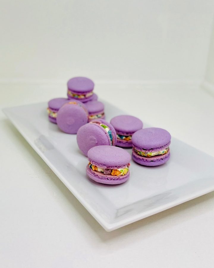 Purple macarons featuring a vibrant, multicolored cereal filling, elegantly displayed on a white rectangular plate.